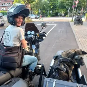 Frau (Eva Strehler) lächelnd auf Motorradgespann, im Beiwagen Hund (Hündin Polly) mit Motorradbrille