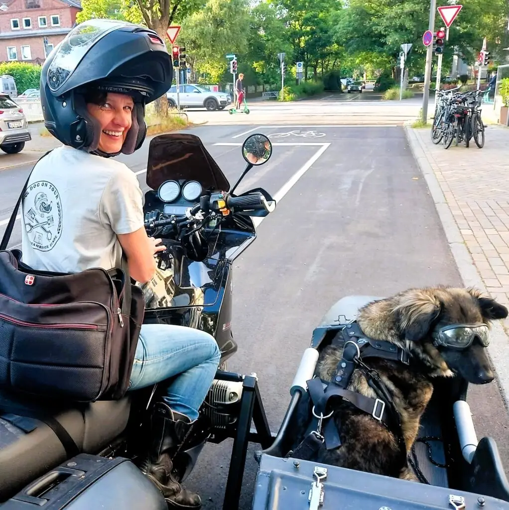 Frau (Eva Strehler) lächelnd auf Motorradgespann, im Beiwagen Hund (Hündin Polly) mit Motorradbrille