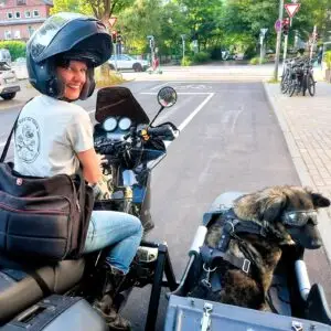 Frau (Eva Strehler) lächelnd auf Motorradgespann, im Beiwagen Hund (Hündin Polly) mit Motorradbrille