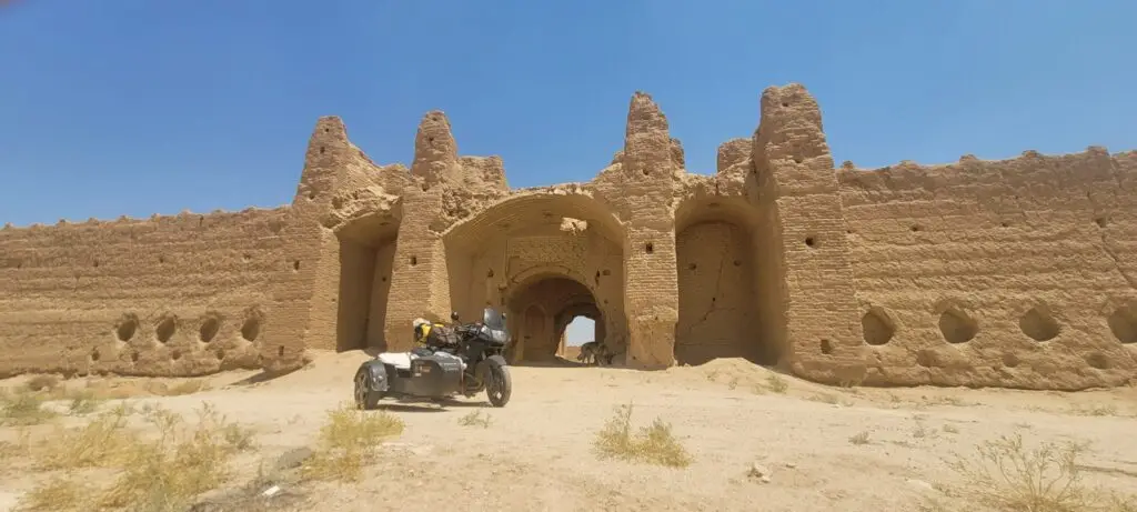 alte Karawanserei im Iran unter blauem Himmel, davor Motorradgespann und Hund