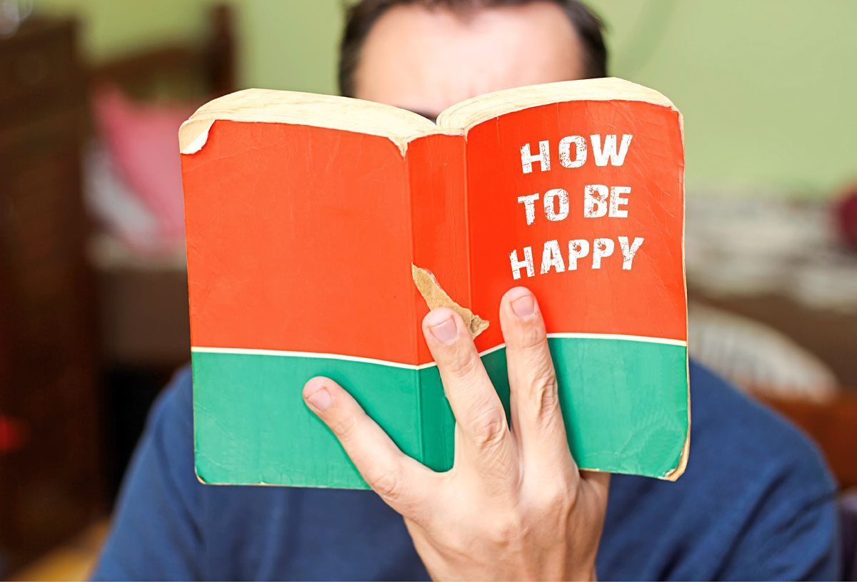 Mann hält Buch "How to be Happy" vors Gesicht
